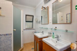 Salle de bain familiale avec douche, toilettes et lavabos.