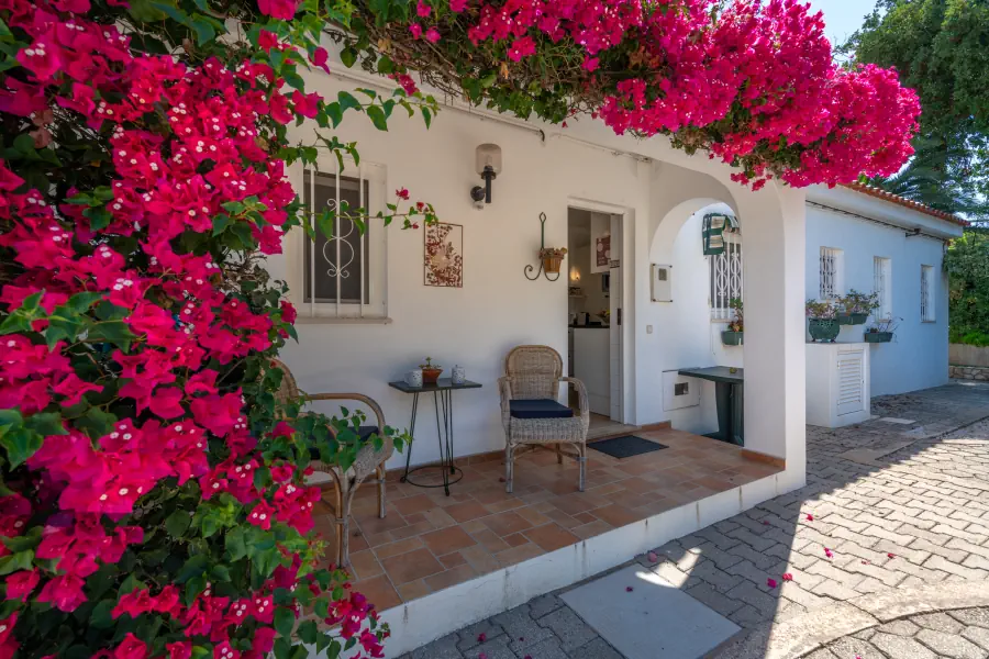 Une terrasse couverte ornée de bougainvilliers roses éclatants, avec deux chaises en rotin et une petite table basse.