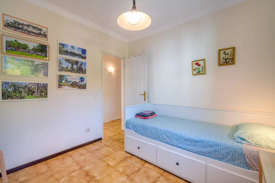Une chambre avec un lit simple bleu muni de tiroirs, une porte ouverte et des cadres décoratifs au mur.