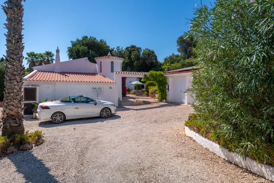Une voiture cabriolet blanche garée devant une villa méditerranéenne avec une cour pavée et un garage.