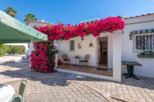 Une terrasse couverte devant une villa blanche, magnifiquement ornée d'un bougainvillier rose grimpant et de deux chaises en rotin.