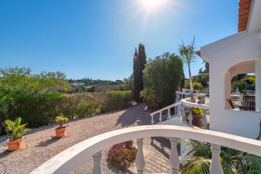 Une vue depuis un balcon en arc avec balustrade blanche donnant sur un grand jardin de gravier et la nature environnante.